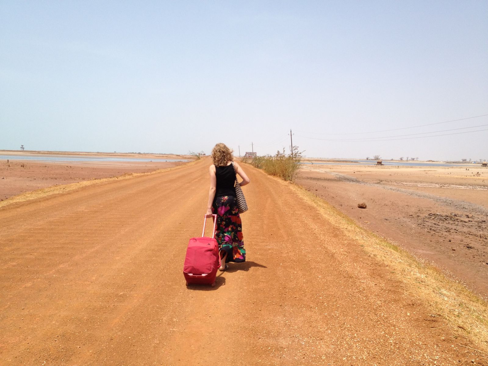 Girl dragging luggage on dusty road in Senegal, Africa.