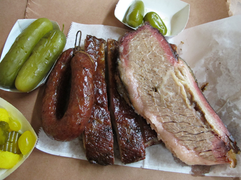 Central Texas BBQ on butcher paper: sausage, ribs, brisket, pickles.