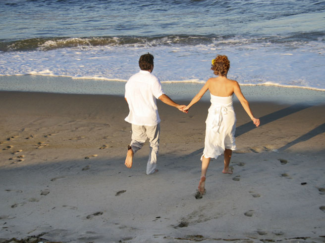 Couple runs toward beach in wedding clothes, Jersey Shore